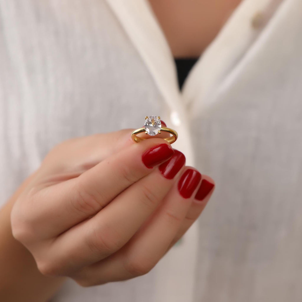 Gold ring with a diamond held by a hand with red nail polish against a white background