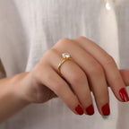 Hand wearing a gold ring with a diamond on a plain background