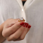Gold ring with a cubic zirconia held by a hand with red nail polish against a white background