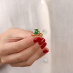Hand wearing a gold ring with a green gemstone against a plain background