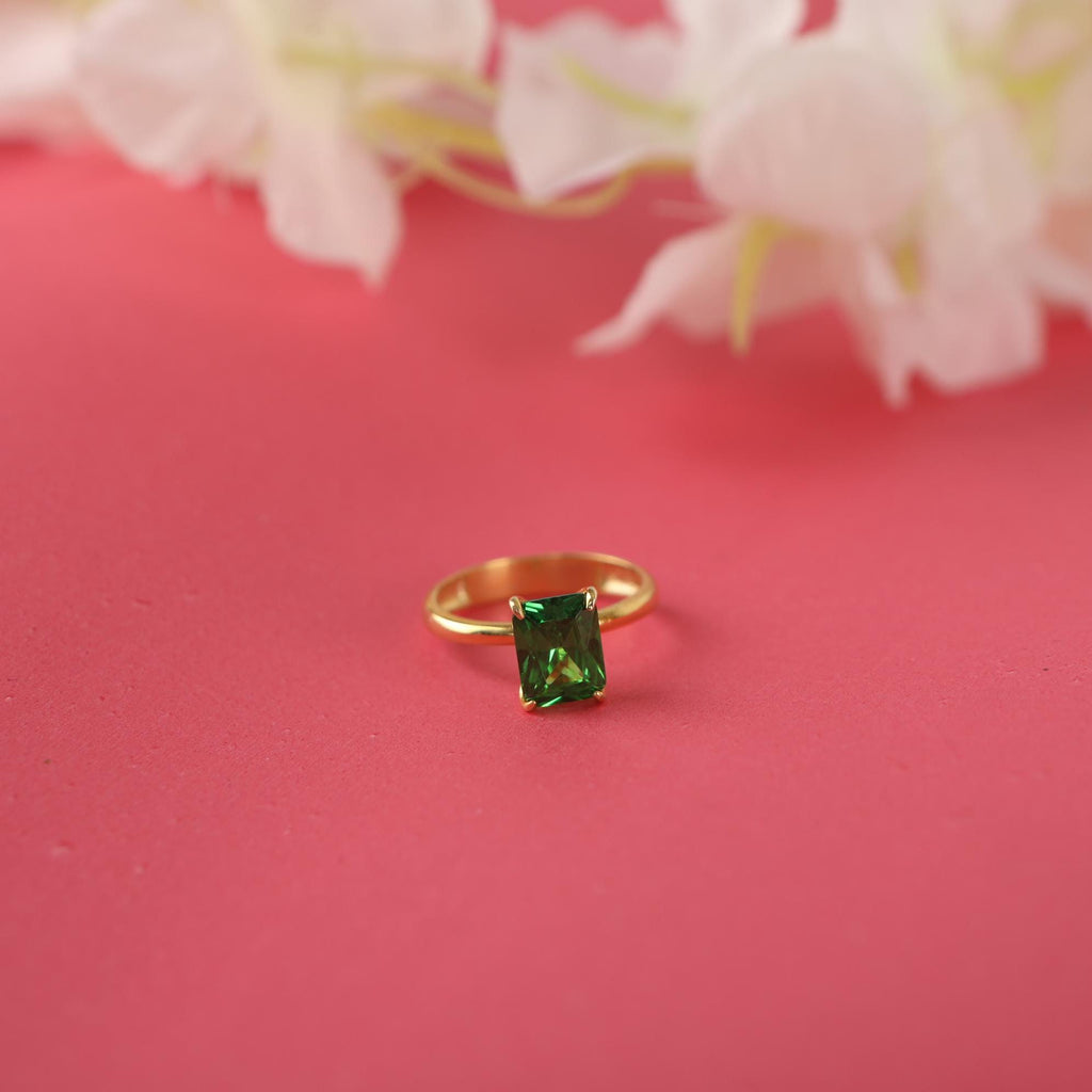 Gold ring with a green gemstone on a pink background with white flowers.
