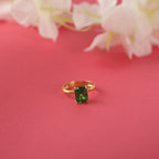 Gold ring with a green gemstone on a pink background with white flowers.