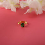 Gold ring with a green gemstone on a pink background with flowers.