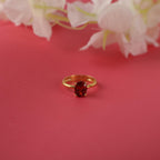 Gold ring with a red gemstone on a pink background with white flowers.