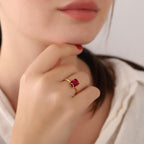 Close-up of a hand wearing a gold ring with a red gemstone, touching the chin.