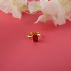 Gold ring with a red gemstone on a pink background with flowers