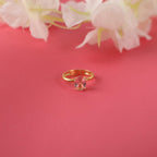 Gold ring with a pink gemstone on a pink background with white flowers.