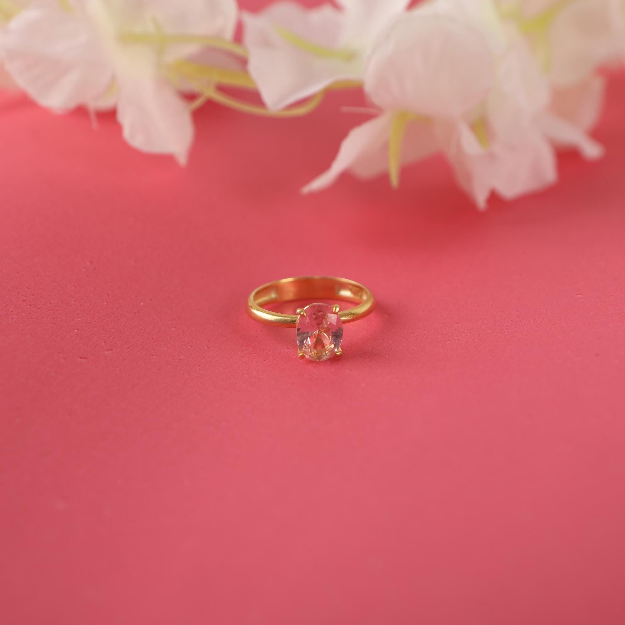 Gold ring with a pink gemstone on a pink background with white flowers.