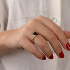 Hand wearing a gold ring with a black gemstone on a neutral background