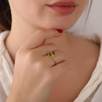 Close-up of a hand wearing a gold ring with a green gemstone, touching the chin.