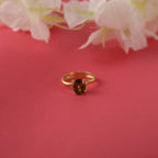 Gold ring with a brown gemstone on a pink background with white flowers.