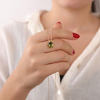Hand holding a gold necklace with a peridot gemstone against a white background