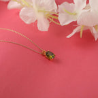 Gold necklace with a green gemstone peridot pendant on a pink background with flowers.