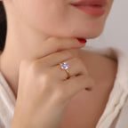Close-up of a hand wearing a gold ring with a purple gemstone, touching the chin.