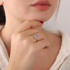 Close-up of a hand wearing a gold ring with a purple gemstone, touching the chin.