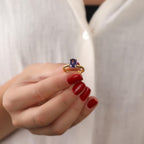 Close-up of a hand wearing a gold ring with a purple gemstone against a white background