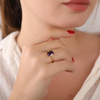 Close-up of a hand wearing a gold amethyst ring with a purple gemstone, blurred background