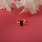 Gold ring with a radiant cut red gemstone on a pink background with white flowers.