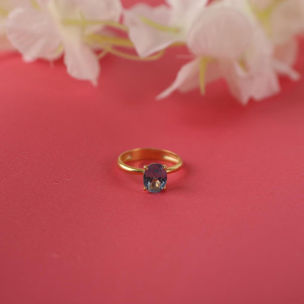Gold ring with a blue gemstone on a red background with white flowers.
