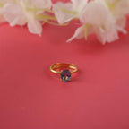 Gold ring with a blue gemstone on a red background with white flowers.