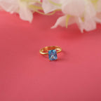 Gold ring with a radiant cut blue gemstone on a pink background with flowers