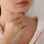 Close-up of a hand wearing a gold ring with a yellow gemstone, touching the chin.