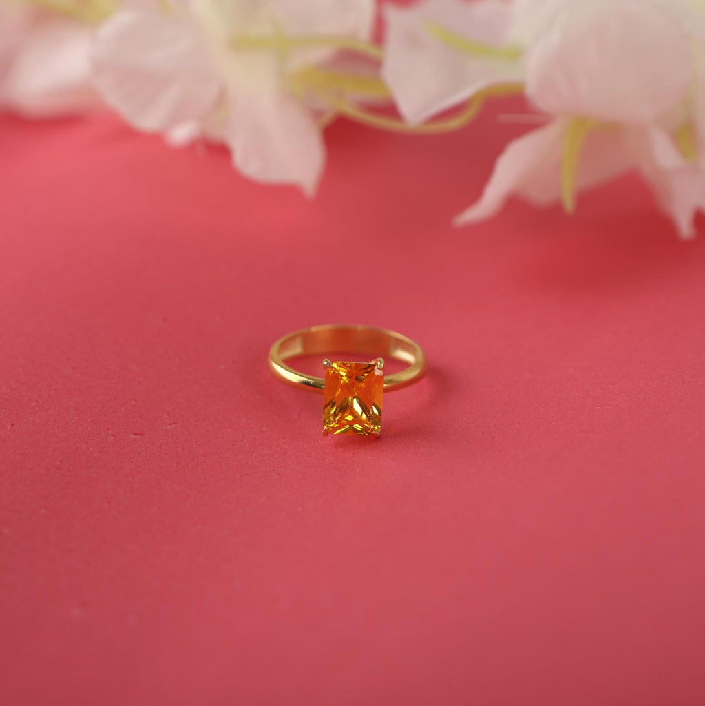 Gold ring with a rectangular yellow gemstone on a pink background with flowers.