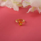 Gold ring with a rectangular yellow gemstone on a pink background with flowers.