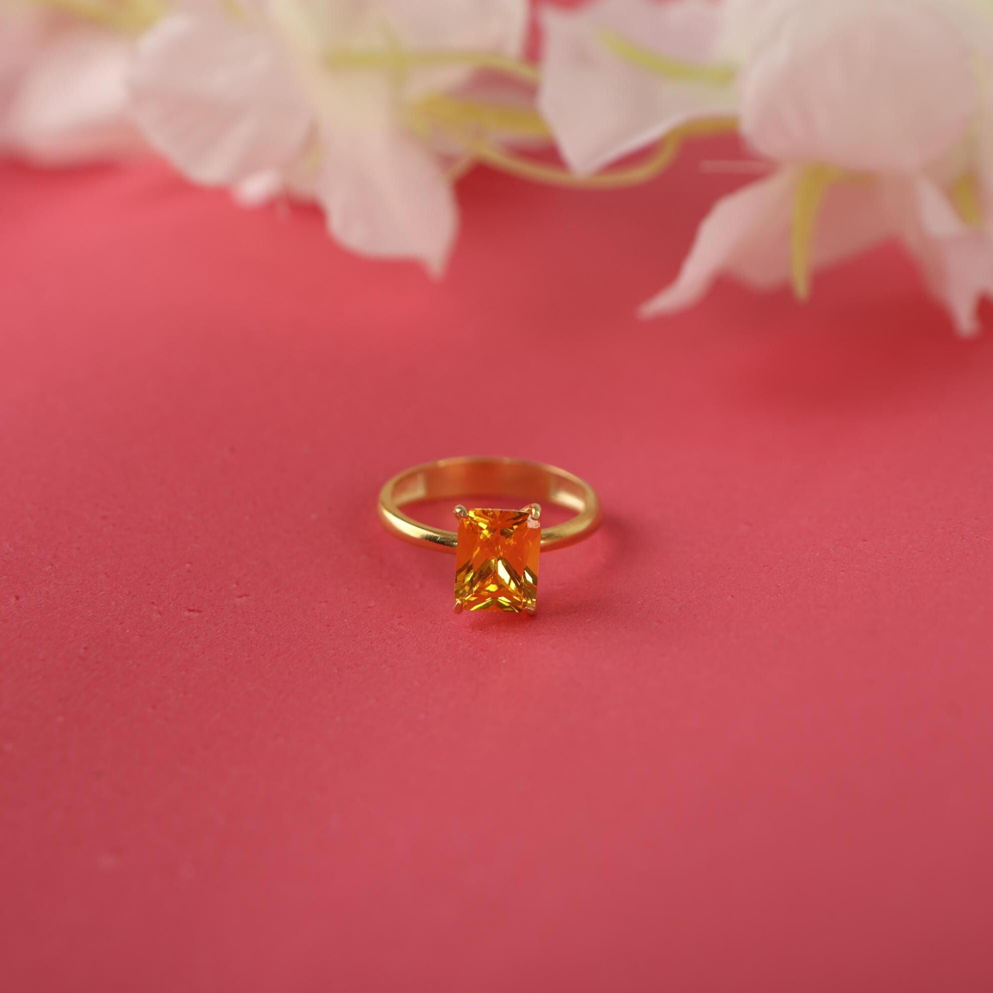 Gold ring with a rectangular yellow gemstone on a pink background with flowers.