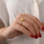 Hand wearing a gold ring with a red nail polish on a neutral background
