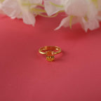 Gold ring with a red gemstone on a pink background with white flowers.