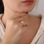 Close-up of a hand wearing a gold ring with a diamond, with a blurred background.