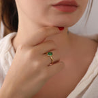 Close-up of a hand wearing a gold ring with a green gemstone, touching the chin.