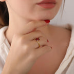 Close-up of a hand wearing a gold ring with a red gemstone, touching the chin.