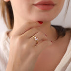 Close-up of a hand wearing a gold ring with a pink gemstone, blurred background