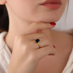 Close-up of a woman's hand wearing a gold ring with a black gemstone, touching her chin.