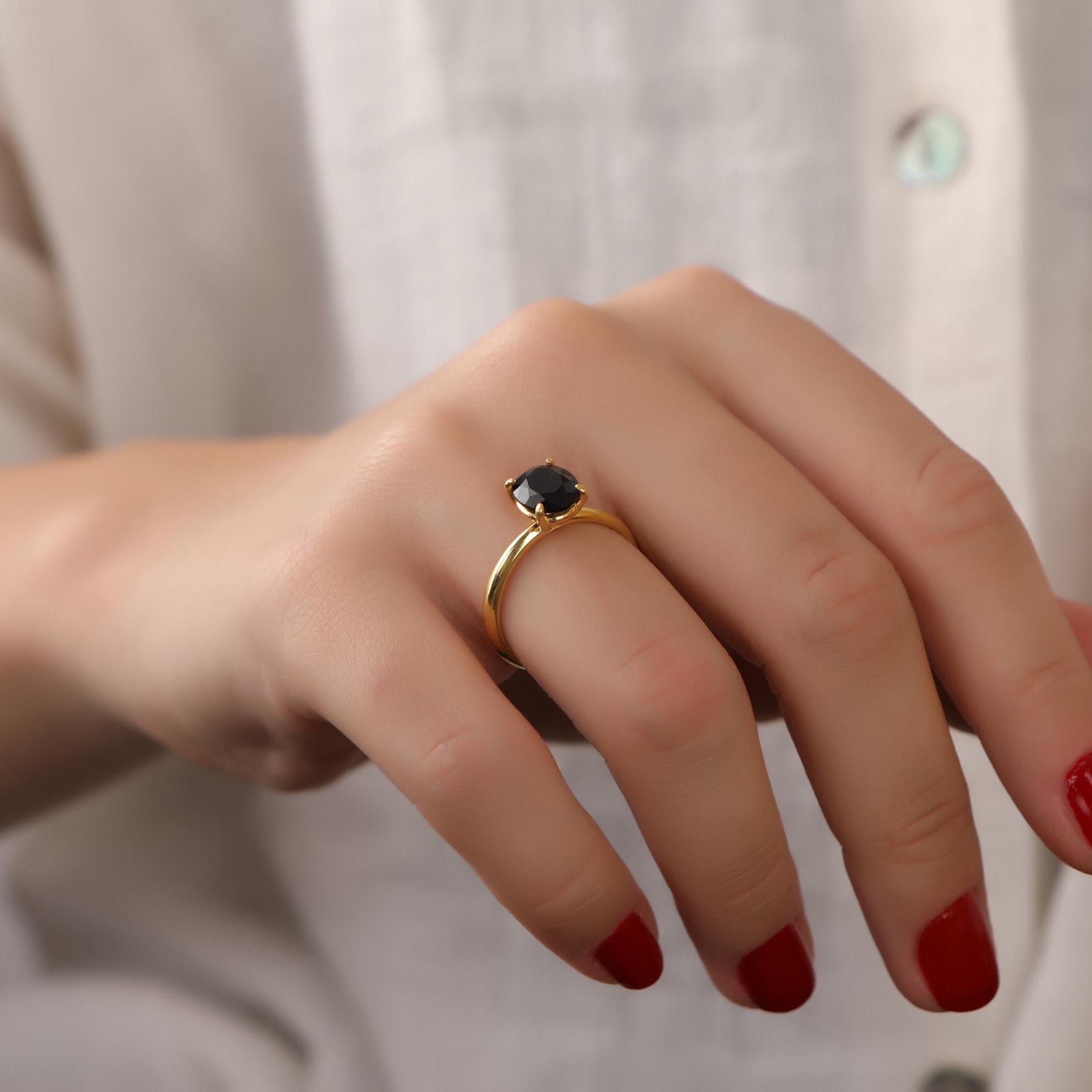Hand wearing a gold ring with a black gemstone against a neutral background