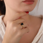 Close-up of a hand wearing a gold ring with a black gemstone, with a blurred background.