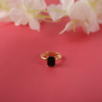 Gold ring with a black gemstone on a pink surface with flowers in the background