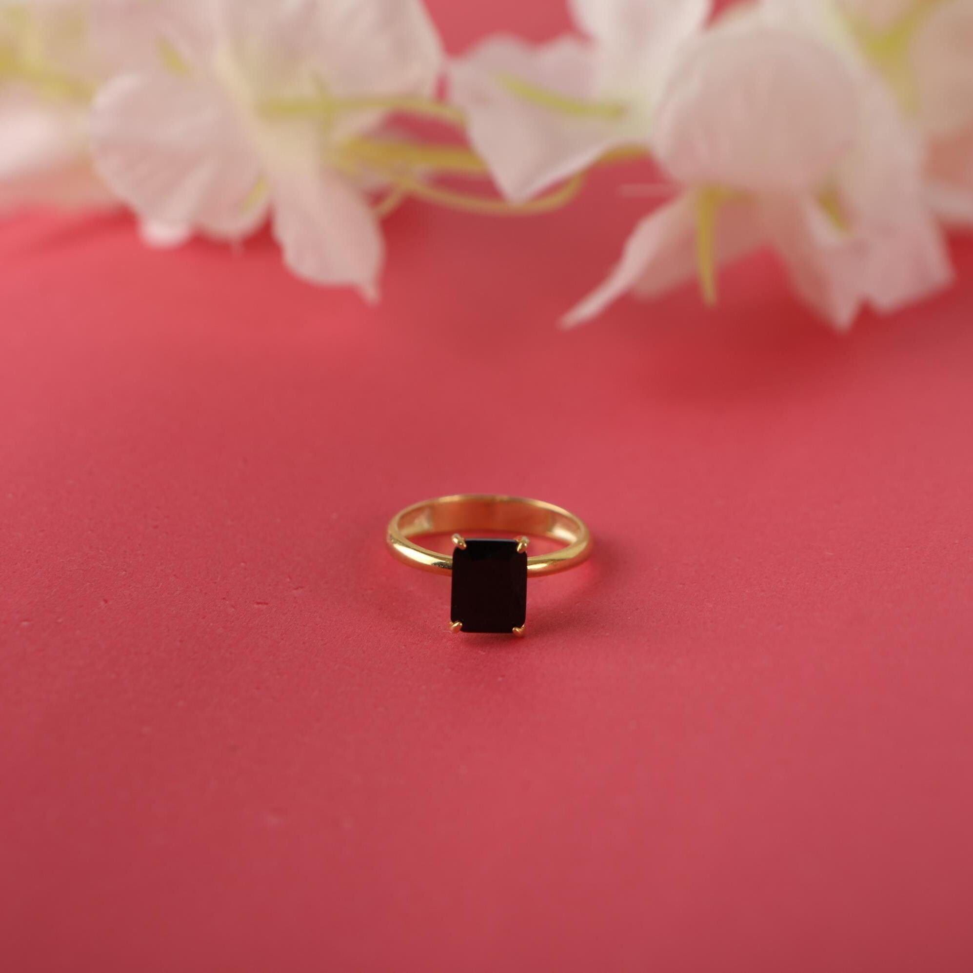 Gold ring with a black gemstone on a pink surface with flowers in the background