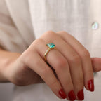 Hand wearing a gold paraiba tourmaline ring on a neutral background