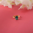 Gold ring with a green gemstone on a pink background with flowers.