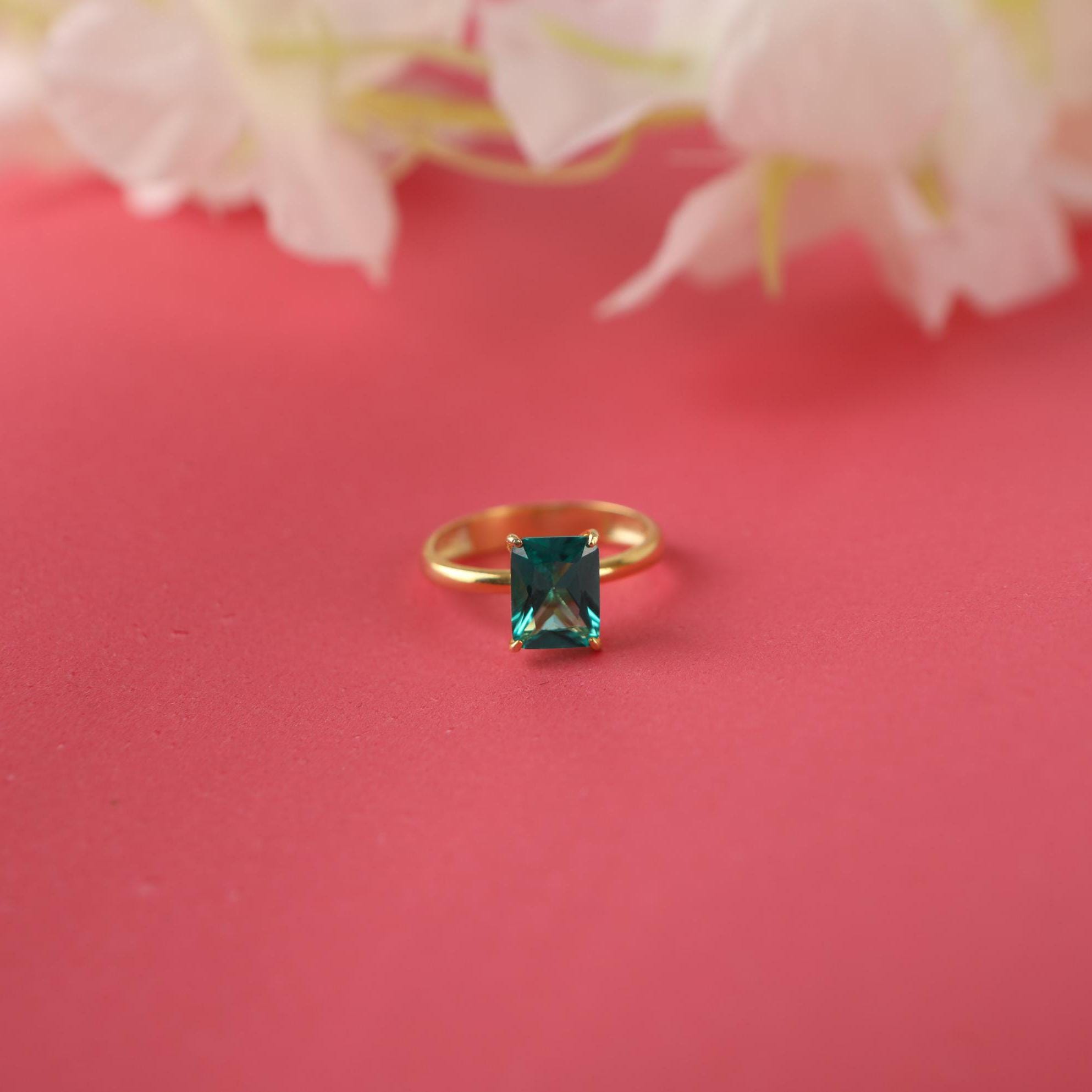 Gold ring with a green gemstone on a pink background with flowers.