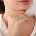 Close-up of a hand wearing a gold ring with a green gemstone, blurred background