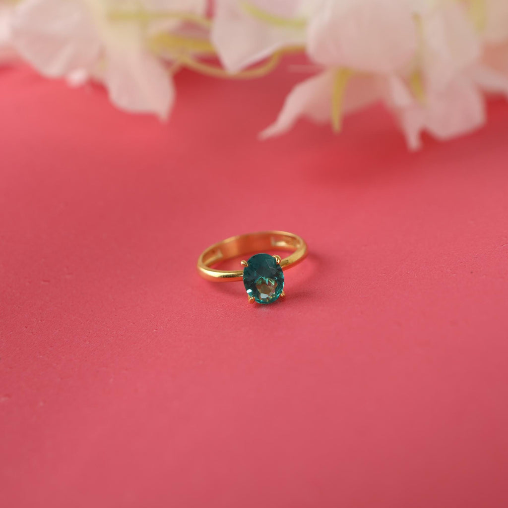 Gold ring with a green gemstone on a pink background with flowers.