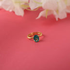 Gold ring with a green gemstone on a pink background with flowers.