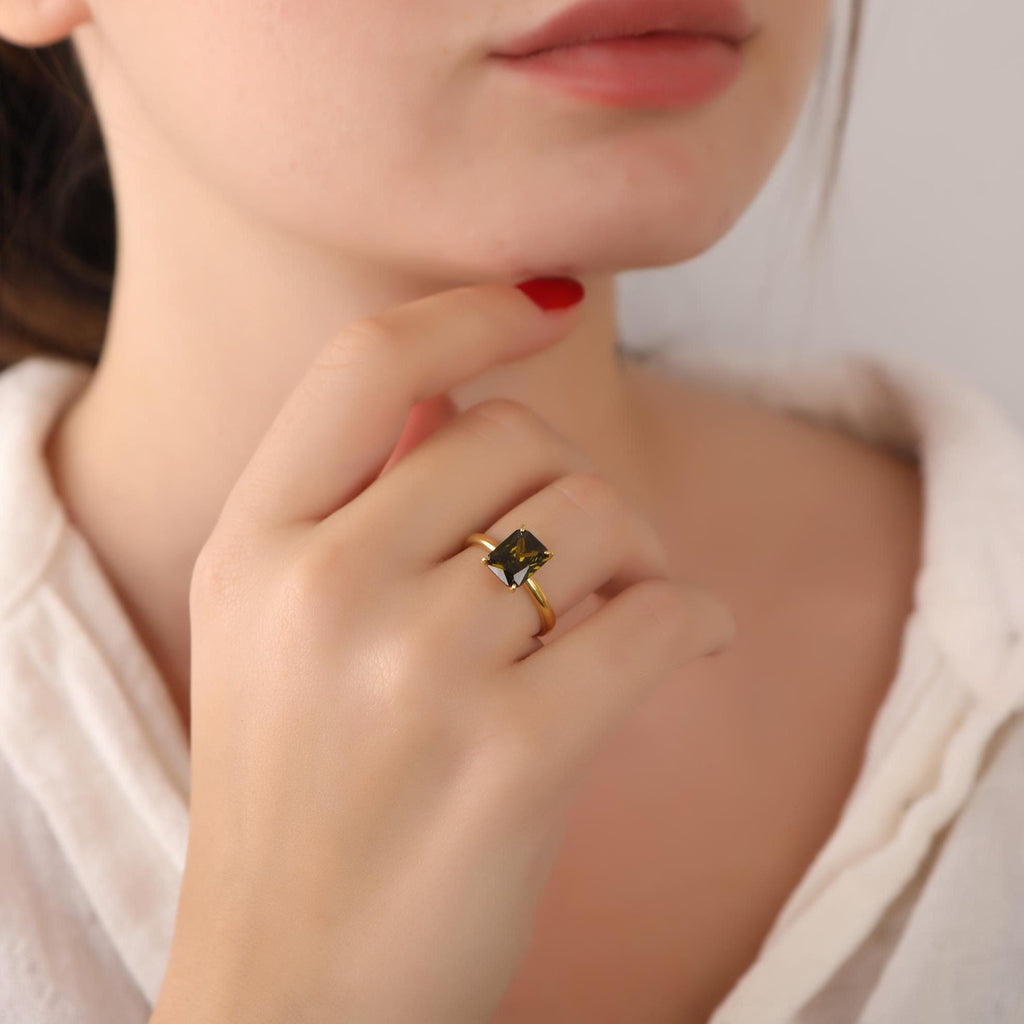 Close-up of a hand wearing a gold ring with a green gemstone, touching the chin.