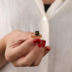 Gold ring with a peridot gemstone held by a hand with red nail polish against a white background