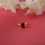 Gold ring with a green gemstone on a pink background with white flowers