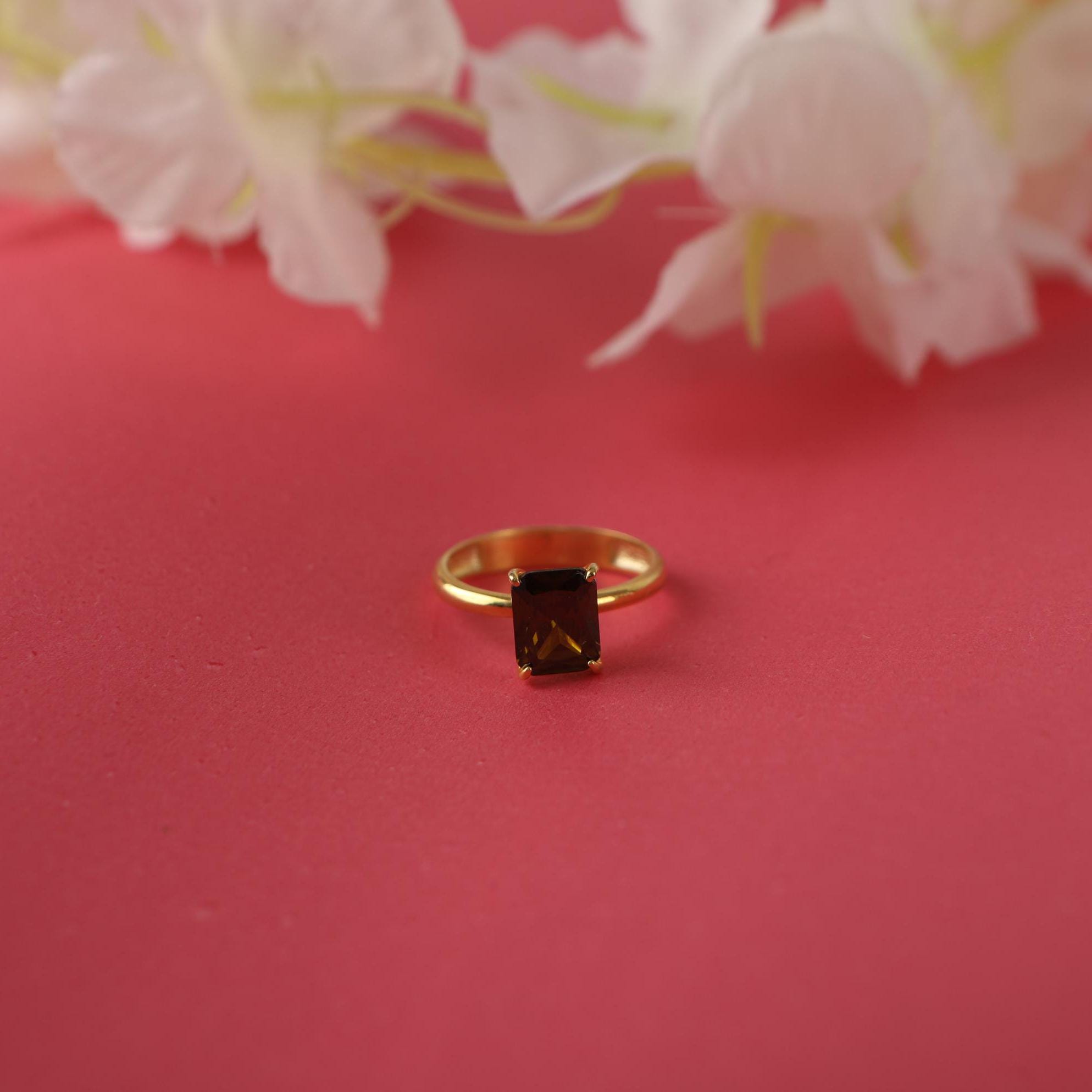 Gold ring with a green gemstone on a pink background with white flowers
